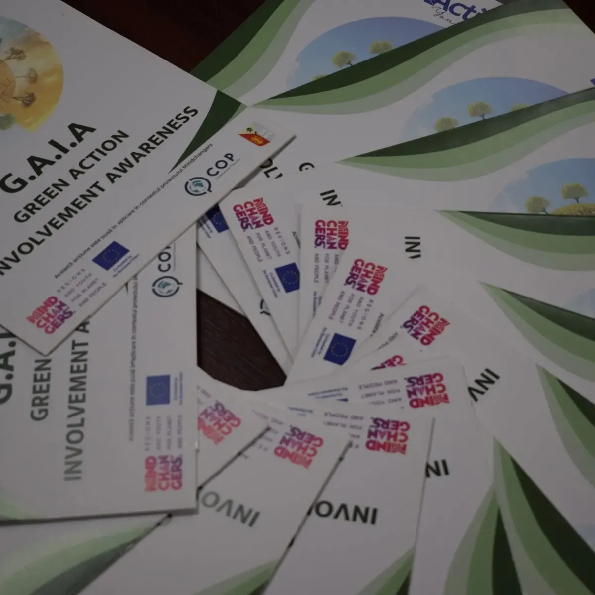 Pliante GAIA și Mindchangers așezate în evantai pe o masă