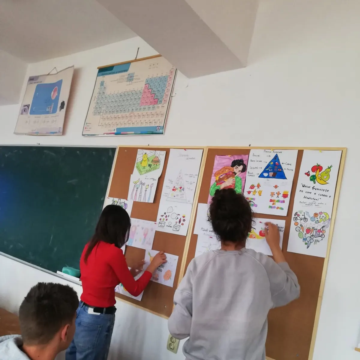 Students arranging their classmates' work on classroom pinboards